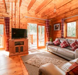 A living room with leather sofas plaid cushions wooden furniture and large windows at Bearscombe View in Modbury
