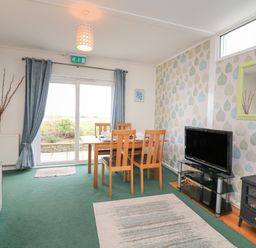 A living room with a dining table and chairs a television on a stand and a small stove at Fairway Lodge in Bigbury-On-Sea