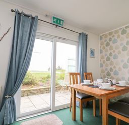 A dining area with a wooden table set with bowls and cups near glass sliding doors at Fairway Lodge in Bigbury-On-Sea