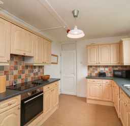 A kitchen with light wood cabinets tiled backsplash oven stovetop microwave toaster and sink at Fairway Lodge in Bigbury-On-Sea