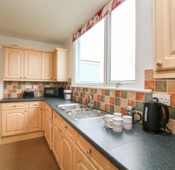 A kitchen with wooden cabinets a countertop with mugs a kettle a microwave and a sink at Fairway Lodge in Bigbury-On-Sea