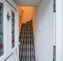 A narrow staircase with striped carpet leading up from a white hallway with a door featuring stained glass panels at Monteva Whitby