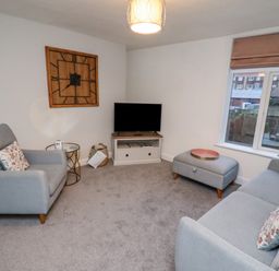 A living room with a sofa armchair ottoman television and wall clock at Monteva in Whitby