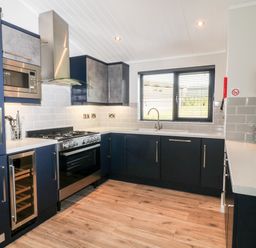A kitchen with blue cabinets a gas stove a microwave a wine cooler a window with blinds and wooden floor at Mayflower Broadwoodwidger near Ashwater