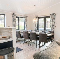 A dining area with a table set for six next to windows and doors with curtains at Mayflower in Broadwoodwidger near Ashwater