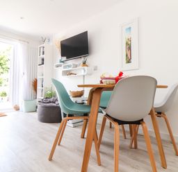 A dining area with a wooden table and chairs next to a wall-mounted TV and bookshelf in a room at Penpoll Little Petherick Creek near Padstow
