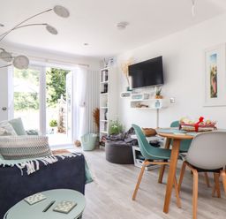 A living room with a sofa dining table chairs and a wall-mounted television at Penpoll Little Petherick Creek near Padstow