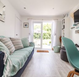 A living room with a sofa covered with a blanket and cushions a green chair and a wall-mounted TV at Penpoll Little Petherick Creek near Padstow