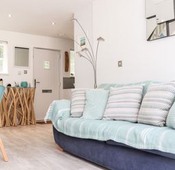 A living room with a sofa covered with blankets and cushions next to a wooden table and a floor lamp at Penpoll Little Petherick Creek near Padstow