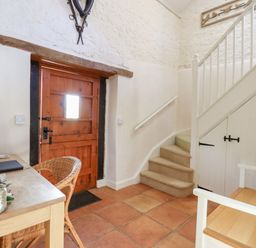 An entryway with a wooden door a small staircase a wooden table and chairs at The Old Barn in Colyton