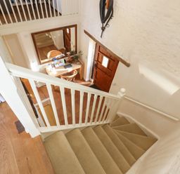 A staircase with beige carpet leading down to a hallway with a wooden door and a wooden table with chairs at The Old Barn in Colyton