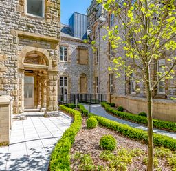 An outdoor courtyard with stone buildings a tree and manicured bushes at Alice House Stone Cross Mansion in Ulverston