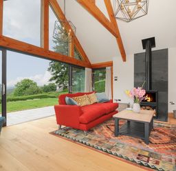 A living room with red sofas and a fireplace with a wood burner at Sandsgate Lodge Spinster's Rock near Chagford