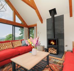 A living room with red sofas a wooden coffee table a fireplace and large windows showing a view at Sandsgate Lodge in Spinster's Rock near Chagford