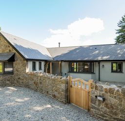 A stone and stucco house with a wooden gate and gravel driveway at Sandsgate Lodge in Spinster's Rock near Chagford