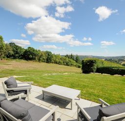 A patio with outdoor chairs and a table overlooking a grassy landscape at Sandsgate Lodge in Spinster's Rock near Chagford
