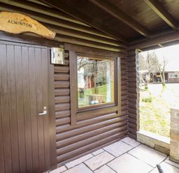 A log cabin entrance with a wooden door and window at Alwinton Lodge in Longframlington