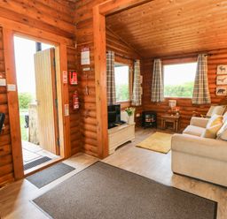 A living room with a sofa, TV, small heater, and a door open to the outside at Alwinton Lodge in Longframlington