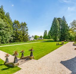A garden with gravel paths green lawn and trees near a stone building at The Elizabeth Suite Stone Cross Mansion Ulverston