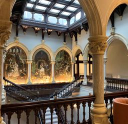 An interior view of a historic building with arched stone columns a painted mural wooden railings and a skylight ceiling at The Alfred Suite Stone Cross Mansion in Ulverston
