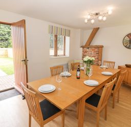 A dining room with a wooden table set with plates glasses a bottle and flowers and an open door leading outside at The Wheat House in Welford-On-Avon
