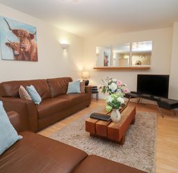 A living room with brown sofas a wooden coffee table with flowers a television and a painting of cows at The Wheat House in Welford-On-Avon