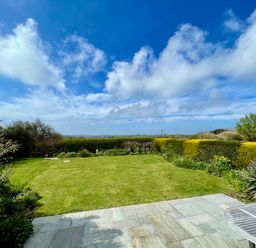 A garden with a lawn and hedges under a blue sky at Alpha in St Minver