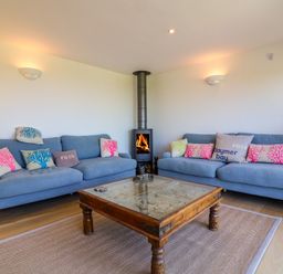 A living room with two blue sofas and a wood stove in the corner at Alpha in St Minver