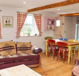 A living room with a patterned sofa red and yellow chairs around a wooden table and a pink wall shelf at Cob Cottage in Kilmore County Wexford