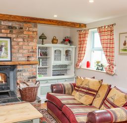 A living room with a brick fireplace a red and patterned sofa a white cabinet and plaid curtains at Cob Cottage in Kilmore County Wexford