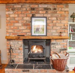 A brick fireplace with a wood burning stove and a basket of firewood in a living room at Cob Cottage in Kilmore County Wexford