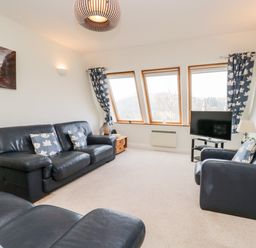 A living room with black leather sofas and armchairs with floral cushions a television and wooden side tables at Rothay in Ambleside