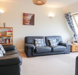 A living room with blue leather sofas a wooden bookshelf and a wooden side table with a window and blue curtains at Rothay in Ambleside