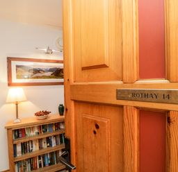 A wooden door with a nameplate reading Rothay 14 opening to a room with a bookshelf a lamp and a framed landscape photo at Rothay in Ambleside