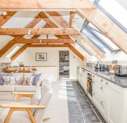An open plan attic kitchen and living area with exposed wooden beams skylights and light furnishings at The Coach House at Thorn Farm Bridford near Moretonhampstead