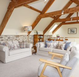 A living room with two sofas, an armchair, wooden beams on the ceiling, and a dining table at The Coach House at Thorn Farm in Bridford near Moretonhampstead