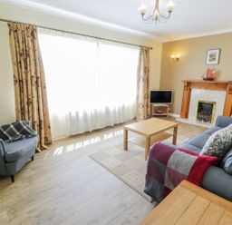 A living room with a gray armchair a sofa a wooden coffee table a fireplace and a television at Ceris in Penrhyndeudraeth
