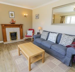 A living room with a blue sofa with cushions a wooden coffee table a red chair a fireplace and a TV at Ceris in Penrhyndeudraeth