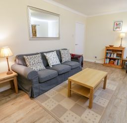 A living room with a gray sofa and cushions a wooden coffee table a wooden side table with a lamp a wooden bookshelf a gray armchair and a framed picture on the wall at Ceris in Penrhyndeudraeth