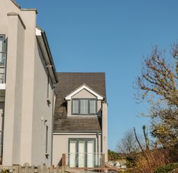 Exterior view of a modern house with balcony and glass railing surrounded by trees and a wooden fence at Seaspray Stoke Fleming Near Dartmouth