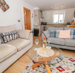 A living room with two sofas a glass coffee table with a bottle and glasses and a kitchen in the background at Seaspray Stoke Fleming Near Dartmouth