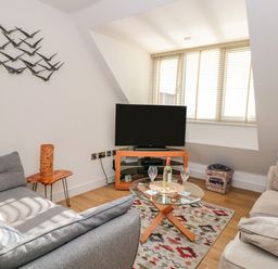A living room with two sofas a glass coffee table with a bottle and glasses and a television at Seaspray in Stoke Fleming Near Dartmouth