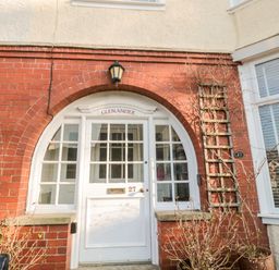 A white front door with glass panels and the number 27 set in a red brick house with an arched entrance at Glenander in Bamburgh