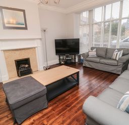 A living room with two gray sofas a wooden coffee table a flat screen tv and a fireplace at Glenander Bamburgh