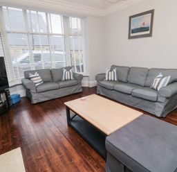 A living room with two gray sofas, a wooden coffee table, a large window with blinds, and a television on a stand at Glenander in Bamburgh