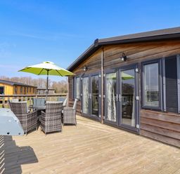 An outdoor wooden deck with a table and wicker chairs under a green umbrella at Skylarks in Fornham St Genevieve near Bury St Edmunds