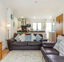 A living room with brown leather sofas and cushions facing a kitchen area with wooden tables at Constantine Bay Cottage in Constantine Bay