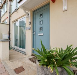 The front entrance of a house with a blue door a large window a plant in a pot and a beige exterior wall at Constantine Bay Cottage in Constantine Bay