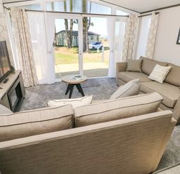 A living room with two sofas a small round table a television and sliding glass doors at Puffin Lodge in Broad Haven