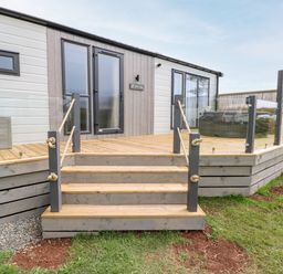 A wooden deck with stairs and rope railings outside a building with glass doors and windows at Puffin Lodge in Broad Haven